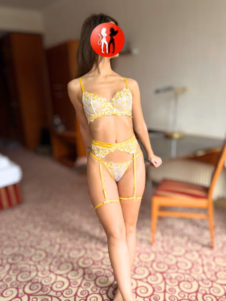 Celina Escort Girl in Dresden steht elegant im Raum, gekleidet in zarte gelbe Spitze. Ihre Pose ist selbstbewusst und zugleich voller weiblicher Sanftheit