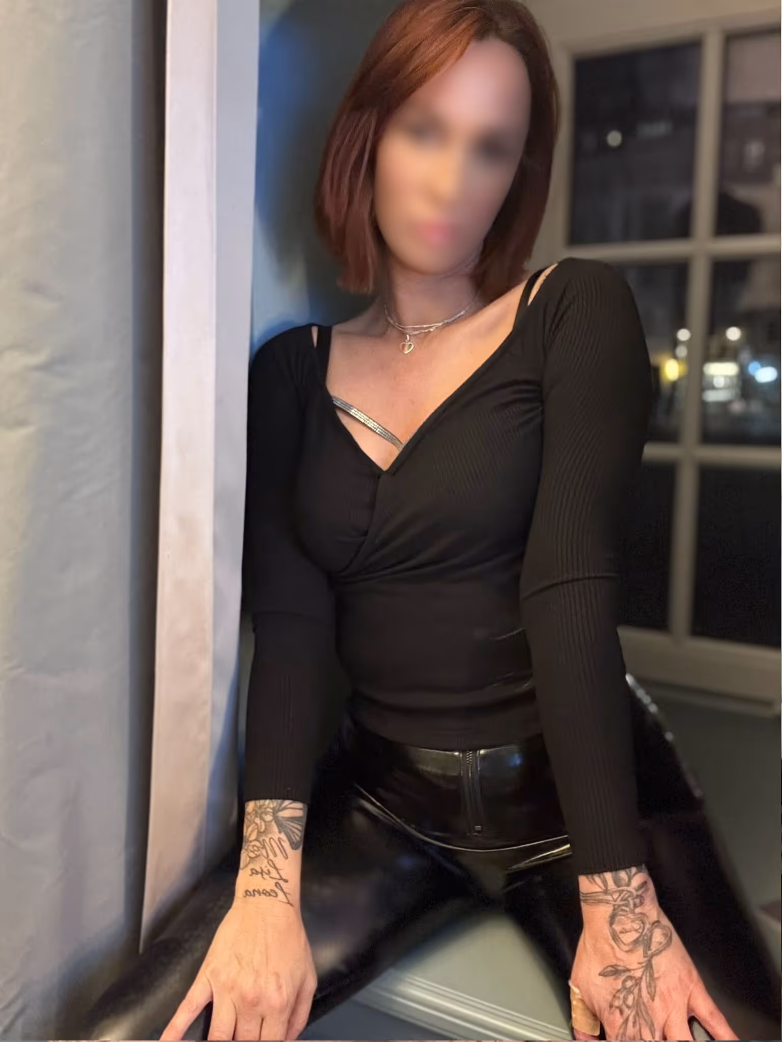 Profilbild aus Emilys Escort Sedcard mit schwarzem enganliegendem Oberteil und Fenster im Hintergrund